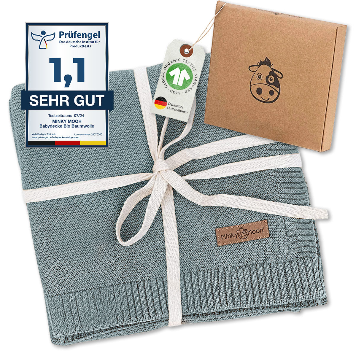 Hochwertige grüne Babydecke aus Bio-Baumwolle, gebunden mit weißem Band, präsentiert neben Prüfsiegel und nachhaltiger Verpackung. Zertifizierte Qualität für sanften Babyschlaf und umweltbewusstes Schenken.