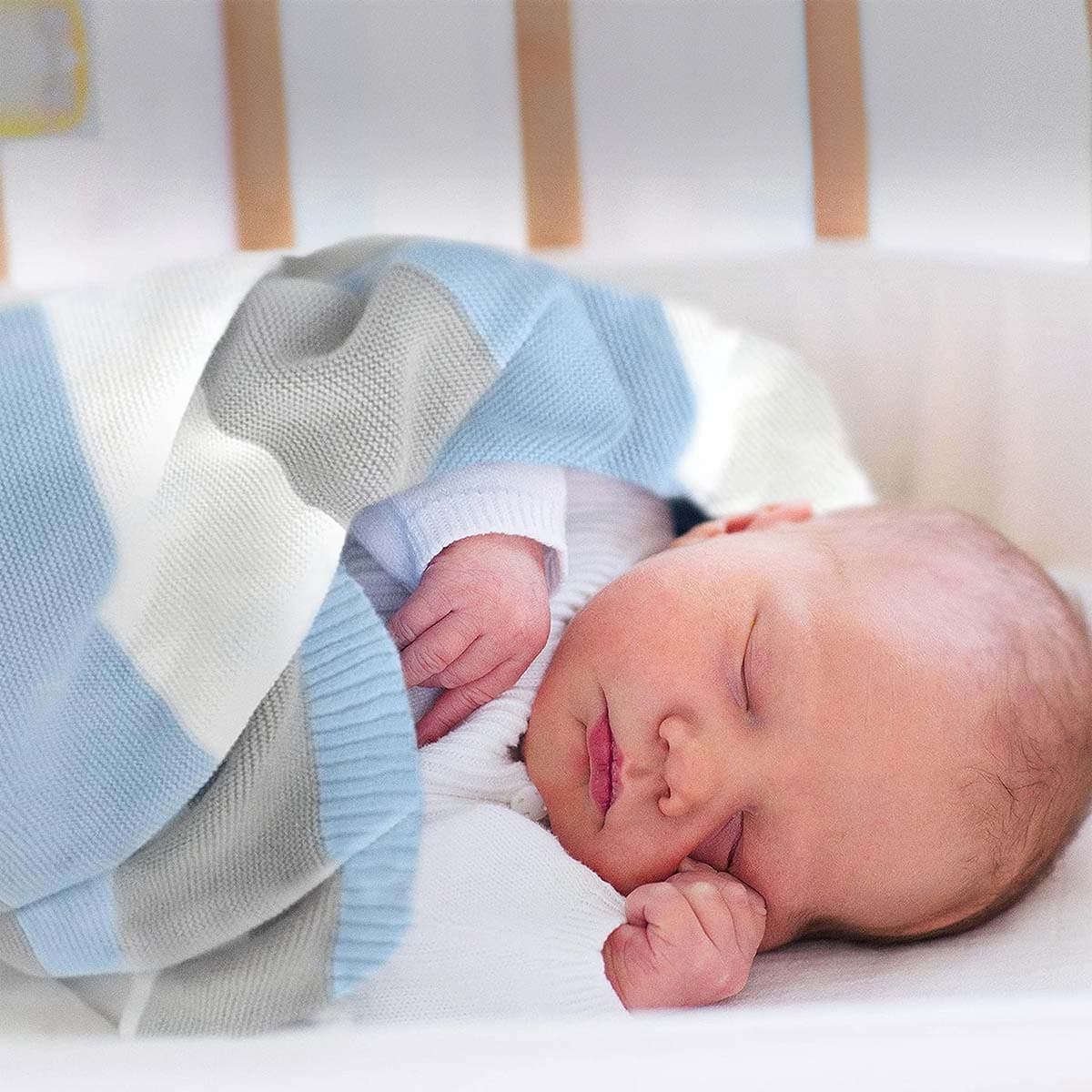 Neugeborenes schläft friedlich eingehüllt in eine blau-weiß-graue gestreifte Bio-Baumwolldecke