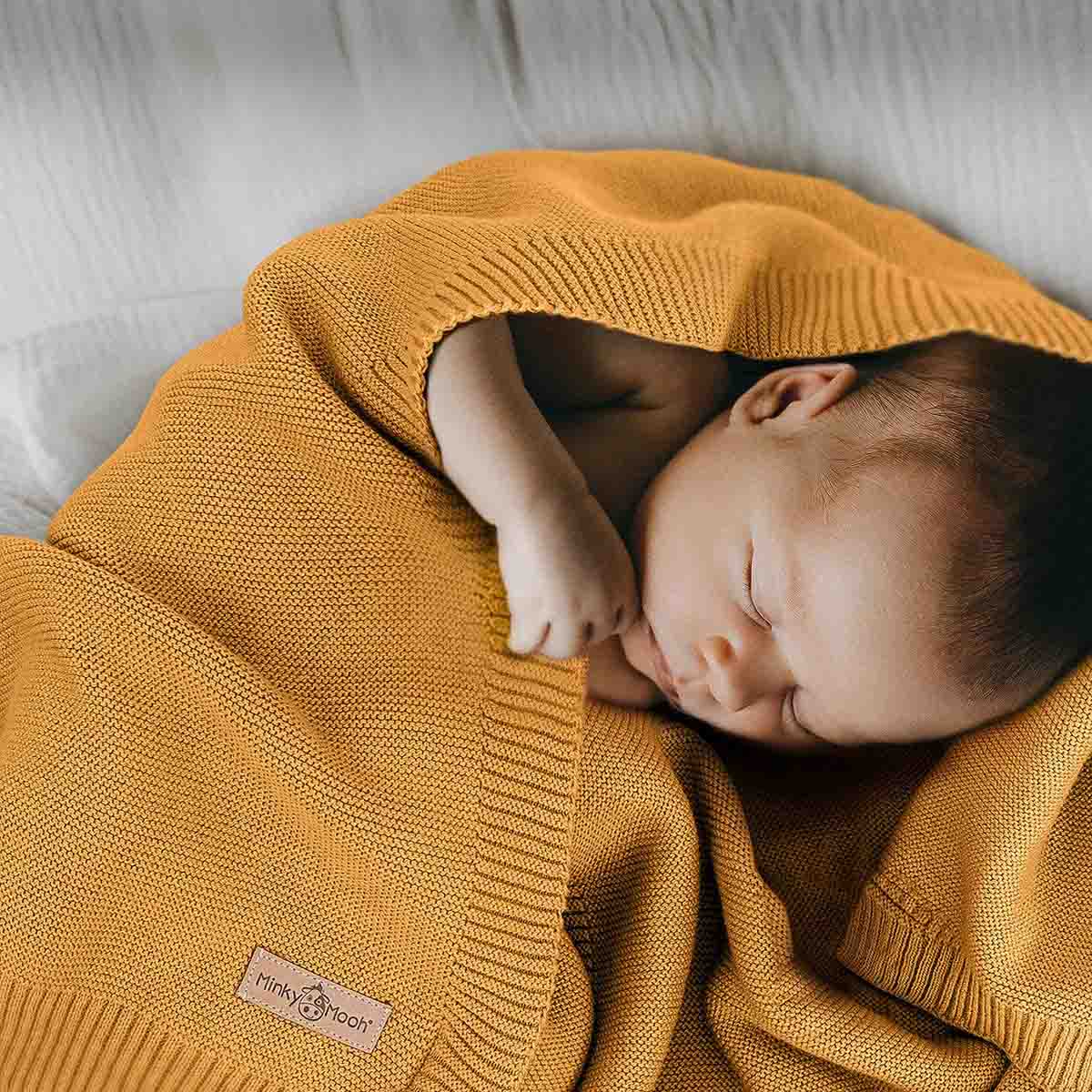 Neugeborenes schläft friedlich eingehüllt in eine dunkel-gelbe Bio-Baumwolldecke.