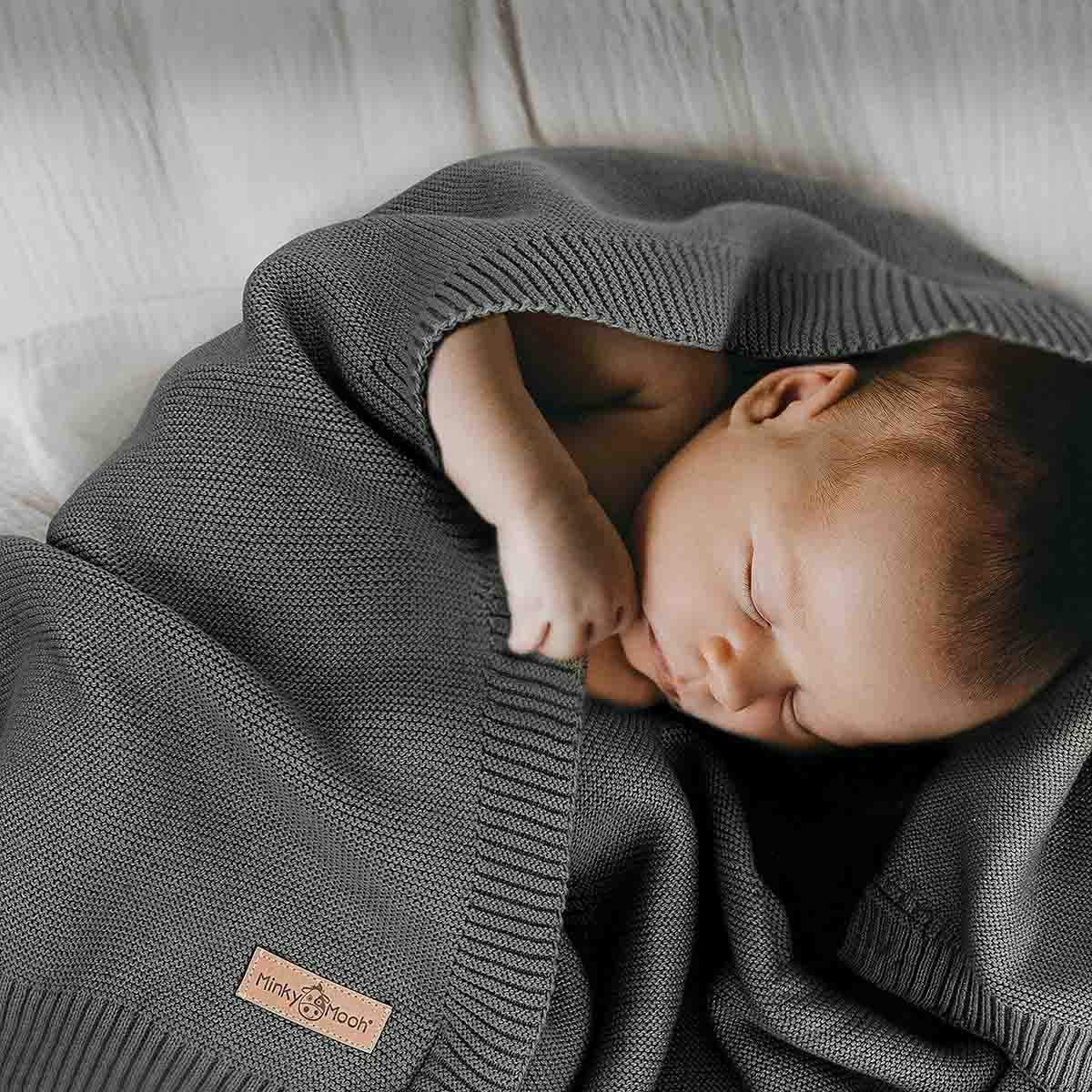 Neugeborenes schläft friedlich eingehüllt in eine dunkel-grüne Bio-Baumwolldecke.