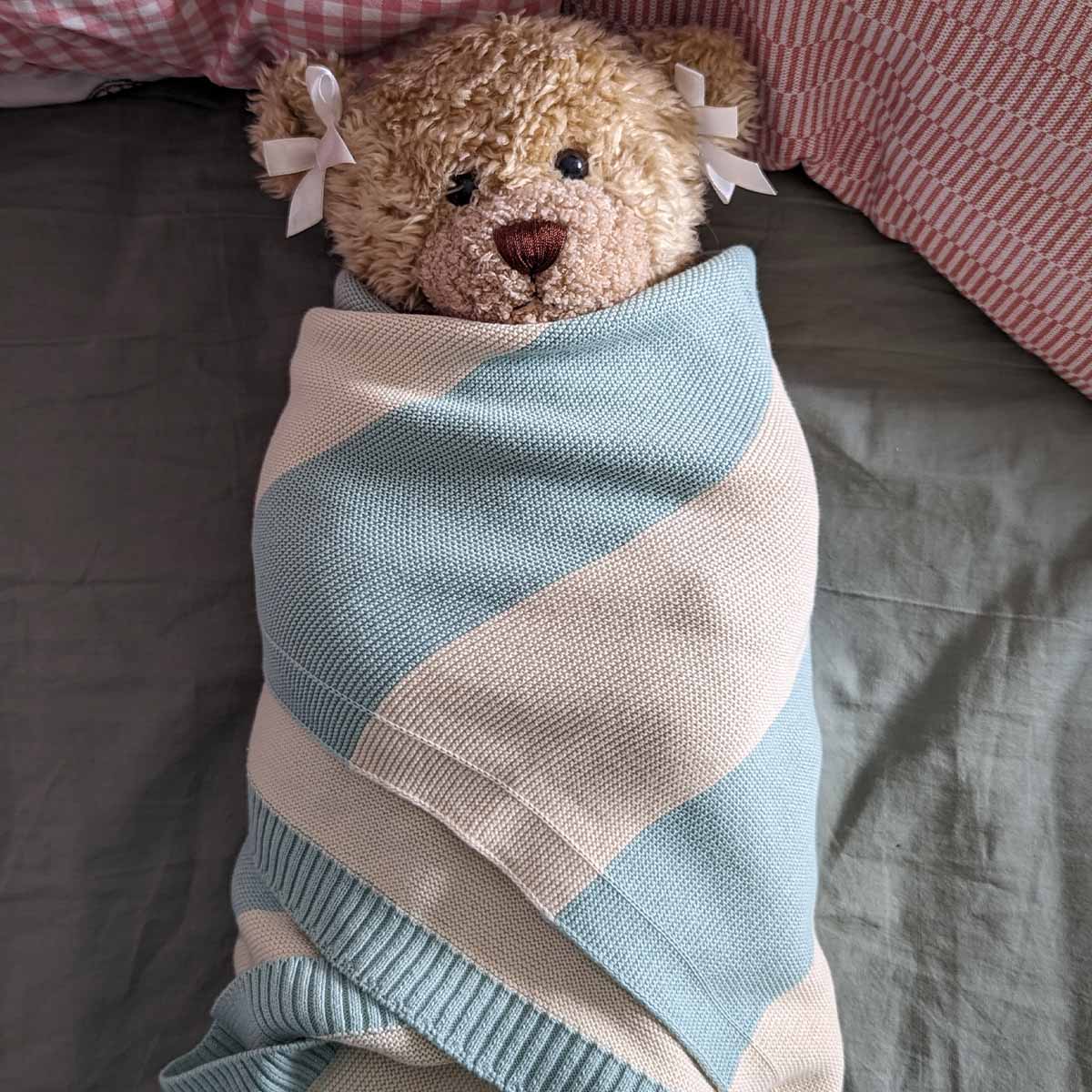 Ein Teddybär eingehüllt in eine mint-natur gestreifte Bio-Baumwolldecke.