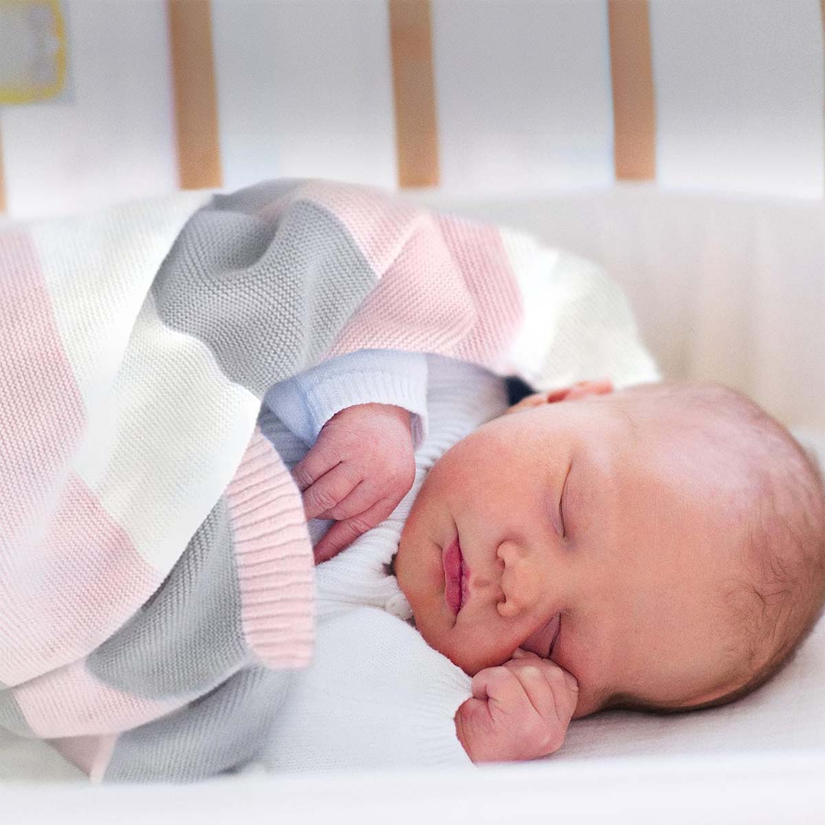 Neugeborenes schläft friedlich eingehüllt in eine rosa-weiß-graue gestreifte Bio-Baumwolldecke.