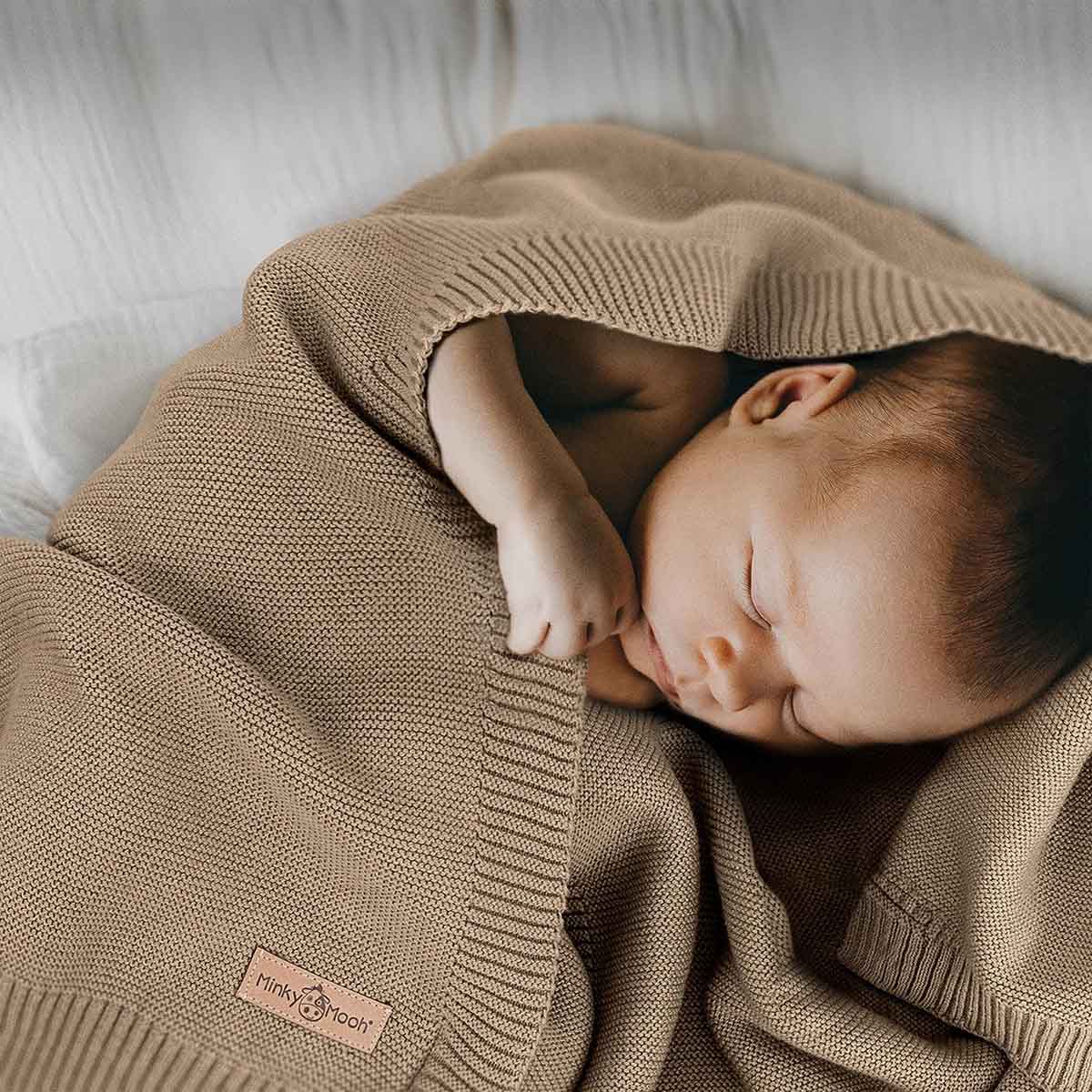 Neugeborenes schläft friedlich eingehüllt in eine taupe farbene Bio-Baumwolldecke.