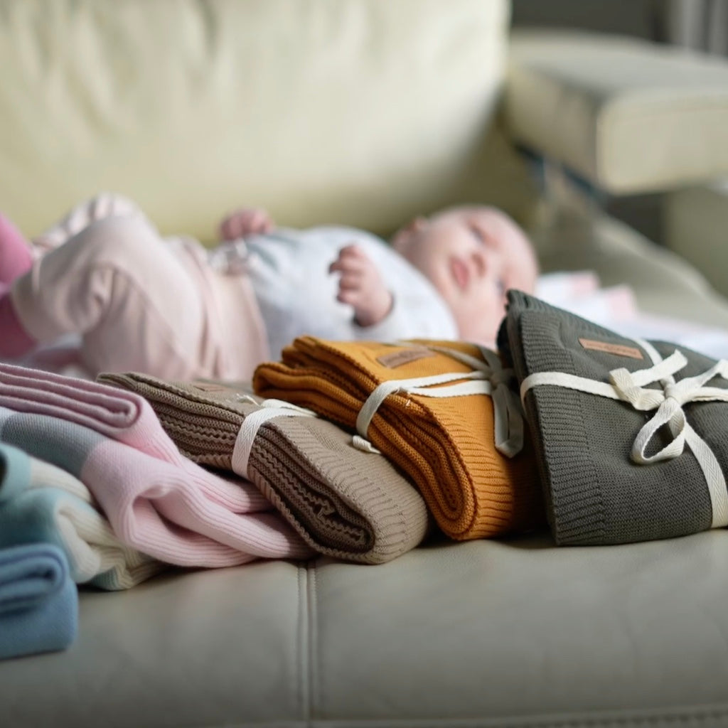 Ein Baby liegt auf einer Couch, umgeben von einem Haufen Decken, in einer gemütlichen und entspannten Atmosphäre.