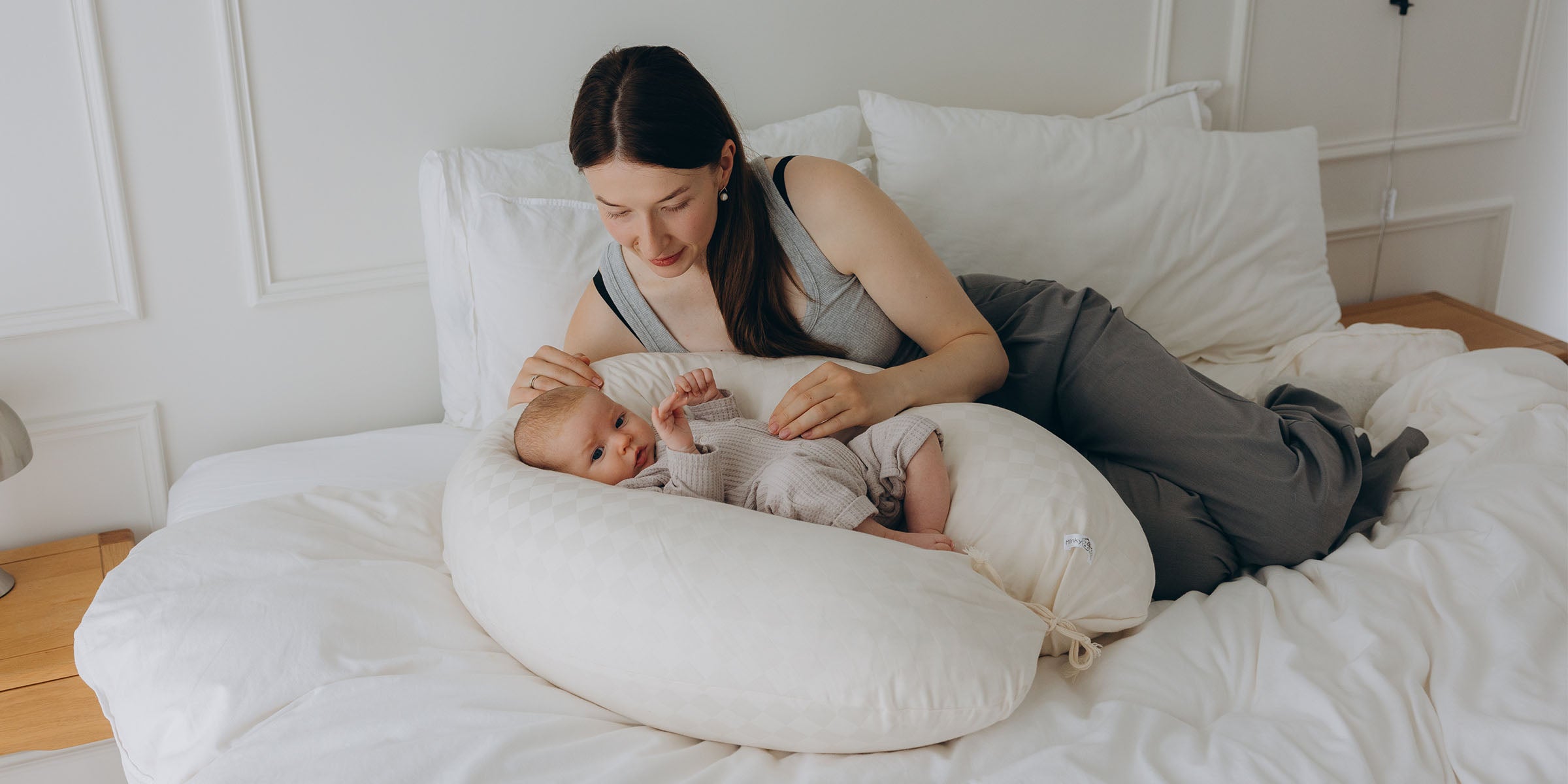 Eine Frau mit einem Baby auf einem weißen Kissen, das als Babynest-Stillkissen aus Kapok geformt ist.